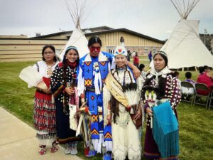 Luella Wagner's students on the Northern Cheyenne Reservation in ceremonial regalia, with teepees in the background.