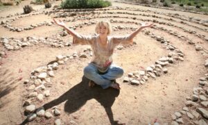 Luella Wagner seated in the center of a labyrinth with outstretched arms.